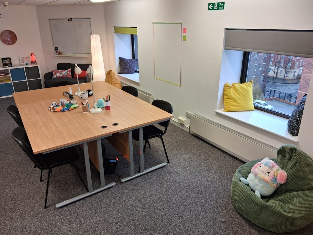 Bright, welcoming meeting room with a large table, chairs, window seats with cushions, and a beanbag with a soft toy.